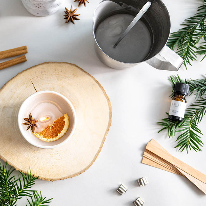 DIY-Tassenkerze mit Holzdocht selber machen – weihnachtliche Duftkerze aus alten Kerzenresten mit Orangenscheibe und Sternanis, umgeben von Duftöl, Holzdochten und Bastelmaterial.