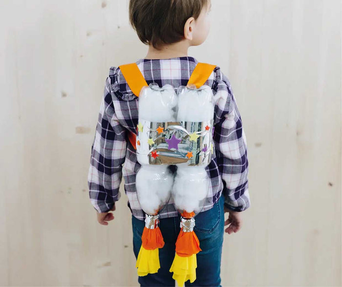 Ein Kind trägt einen selbst gebastelten Raketenrucksack aus zwei PET-Flaschen auf dem Rücken. Der DIY-Rucksack mit silberner Folie, bunten Sternen, orangefarbenen Trägern und Papierflammen eignet sich ideal zum Verkleiden, Spielen und Basteln.