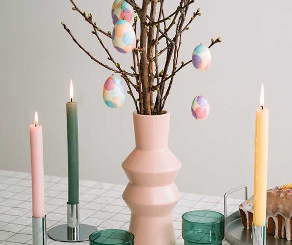Osterbaum mit pastellfarbenen, bunt verzierten Ostereiern in einer rosa Vase. Kerzen und Frühlingsdekoration schaffen eine festliche Osterstimmung.