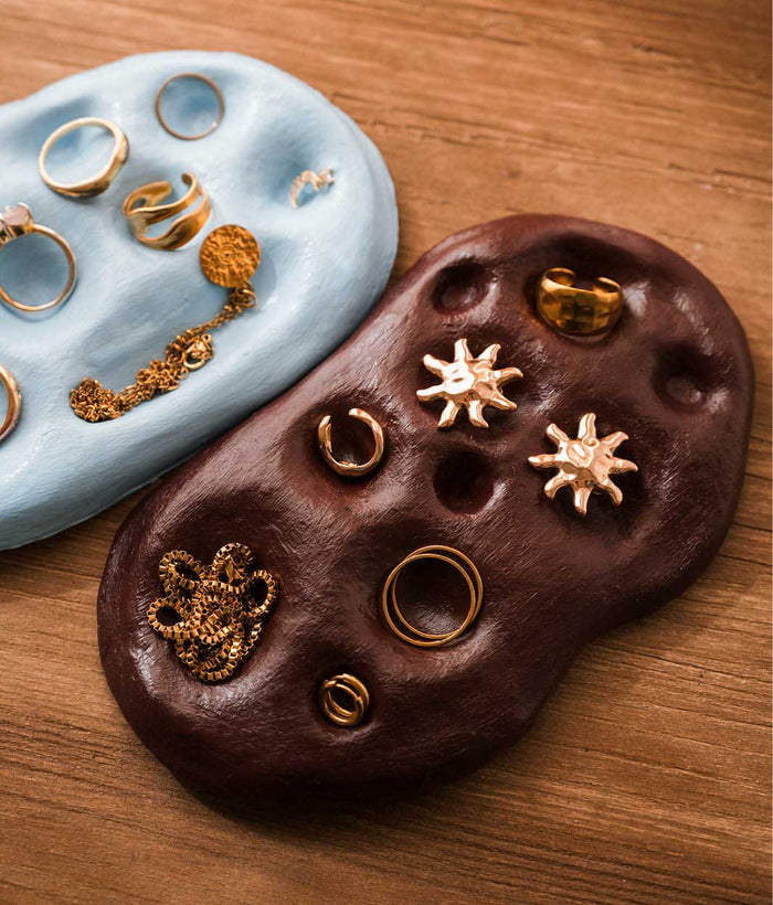 Nahaufnahme einer dunkelbraunen, selbst gemachten Schmuckschale mit Mulden für goldene Ringe, Ohrringe in Sonnenform und eine Kette