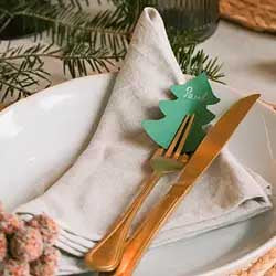 Grüner Tannenbaum als selbst gebastelte Platzkarte mit Namensbeschriftung steckt dekorativ in einer Serviette auf einem festlich gedeckten Weihnachtstisch.