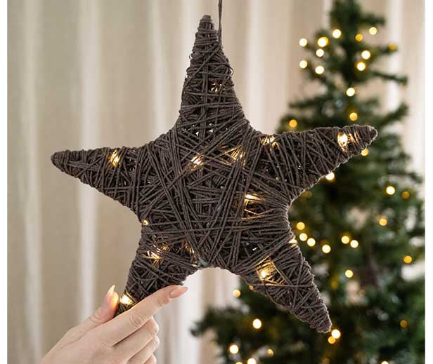 Selbstgemachter Stern aus Schnur mit integrierter LED-Lichterkette als stimmungsvolle Weihnachtsdekoration vor einem geschmückten Weihnachtsbaum.