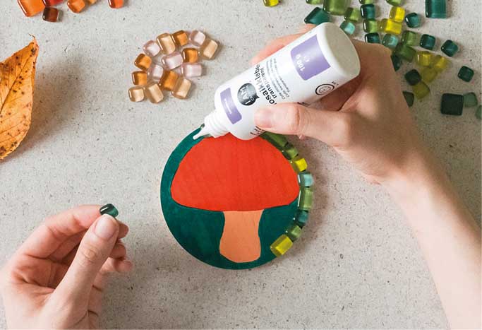 Mosaiksteine werden auf bemalten Holzuntersetzer mit Pilzmotiv geklebt